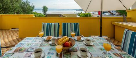 A breakfast table with a view of the sea, yellow walls, and striped cushions.