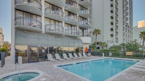 A hotel with a swimming pool, lounge chairs, and a glass-enclosed building with balconies.