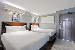 A hotel room with two beds, a door, and a window with blinds.