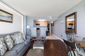 A living room with a sofa, two chairs, a table, and a kitchen in the background.
