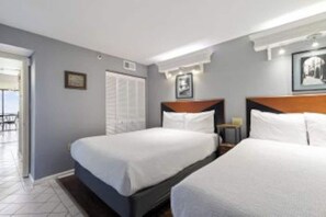 Quarto de hotel com duas camas, cabeceira de madeira, quadro emoldurado na parede e porta para uma varanda.