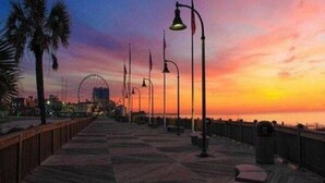 A boardwalk with street lamps and a Ferris wheel in the background during sunset.