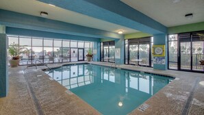 An indoor swimming pool with clear glass walls, a tiled floor, and a lifeguard sign.