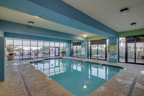 Une piscine intérieure avec des parois en verre transparent, un sol carrelé et un panneau indiquant la présence d’un sauveteur.