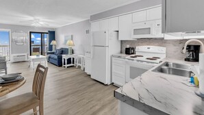 Une cuisine moderne avec des meubles blancs, une cuisinière et un évier. On y trouve également un coin repas avec une table et des chaises.