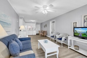 Un salon avec un canapé, une table basse, un téléviseur et un ventilateur de plafond.