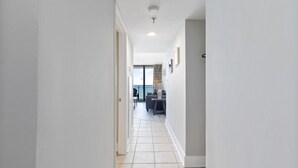 A hallway with a tiled floor leading to a living area with a sofa and a table. - Ocean Forest Plaza Condos 🍹 Close to the beach 🍹 (Myrtle Beach)