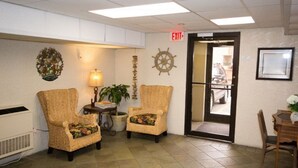 A lobby with wicker chairs, a lamp, a ship's wheel decoration, and an exit sign.