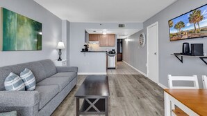 Ein modernes Apartment mit grauem Sofa, einem Couchtisch, einer Küchenzeile und einem Esstisch.