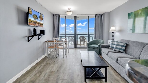 Ein modernes Wohnzimmer mit einer Couch, einem Couchtisch, einem an der Wand montierten Fernseher und einem Balkon mit Meerblick.