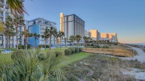 Um hotel à beira-mar com vários edifícios altos, uma praia de areia e um calçadão de madeira.