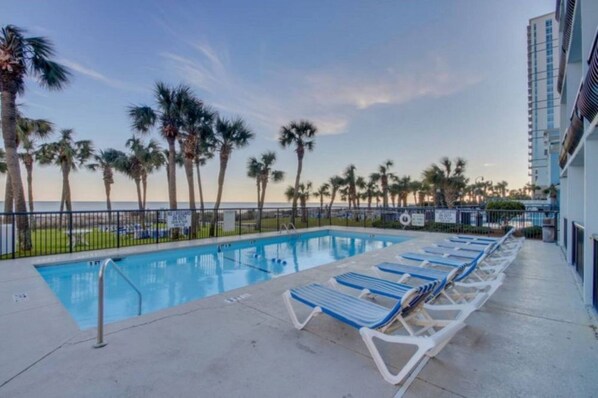 A swimming pool with lounge chairs, palm trees, and a view of the ocean.