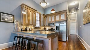 Una cocina con armarios de madera, una isla central con taburetes, electrodomésticos de acero inoxidable e iluminación colgante.