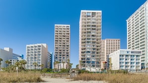 Un hotel frente a la playa con varios edificios de gran altura, con balcones y una playa de arena en primer plano.
