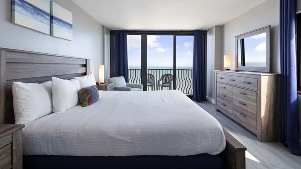 Un dormitorio amplio con una cama grande, un aparador, un televisor y un balcón con vistas al océano.