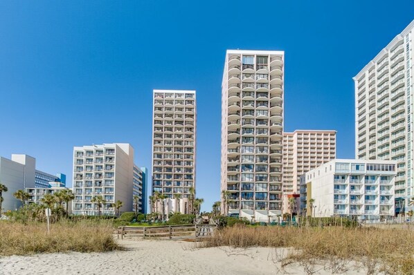 A beachfront hotel with multiple high-rise buildings, featuring balconies and a sandy beach area.
