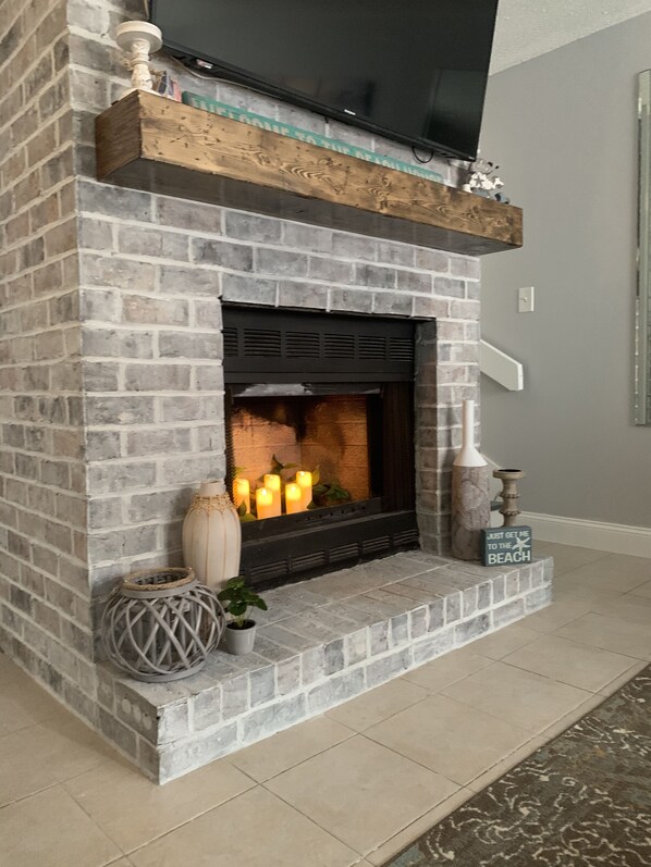 A fireplace with a brick facade, a flat-screen TV mounted above it, and decorative items like candles and vases on the mantel.