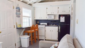A compact kitchen with white cabinets, a stove, a microwave, and a refrigerator. There is a small dining area with two chairs and a table. - 1 bedroom cottage with ac, steps to the beach! (Dennis Port)