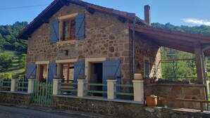 A stone house with a sloped roof, wooden shutters, and a small porch.