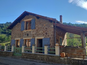 A stone house with a sloped roof, wooden shutters, and a small porch.