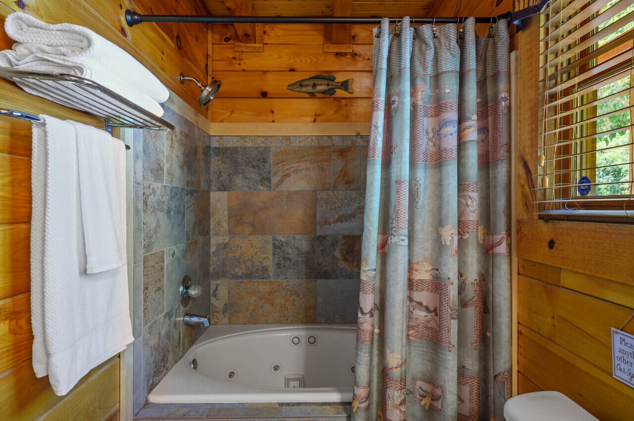 A bathroom with a bathtub, wooden walls, and a shower curtain with a fish pattern.