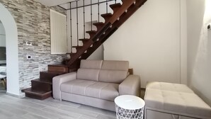 A modern living room with a beige sofa, a small round side table, and a staircase with wooden railings. - Nemo's Home (Arcola)