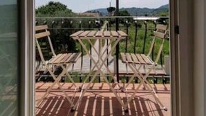 A balcony with wooden chairs and a table, overlooking a hilly landscape. - Nemo's Home (Arcola)