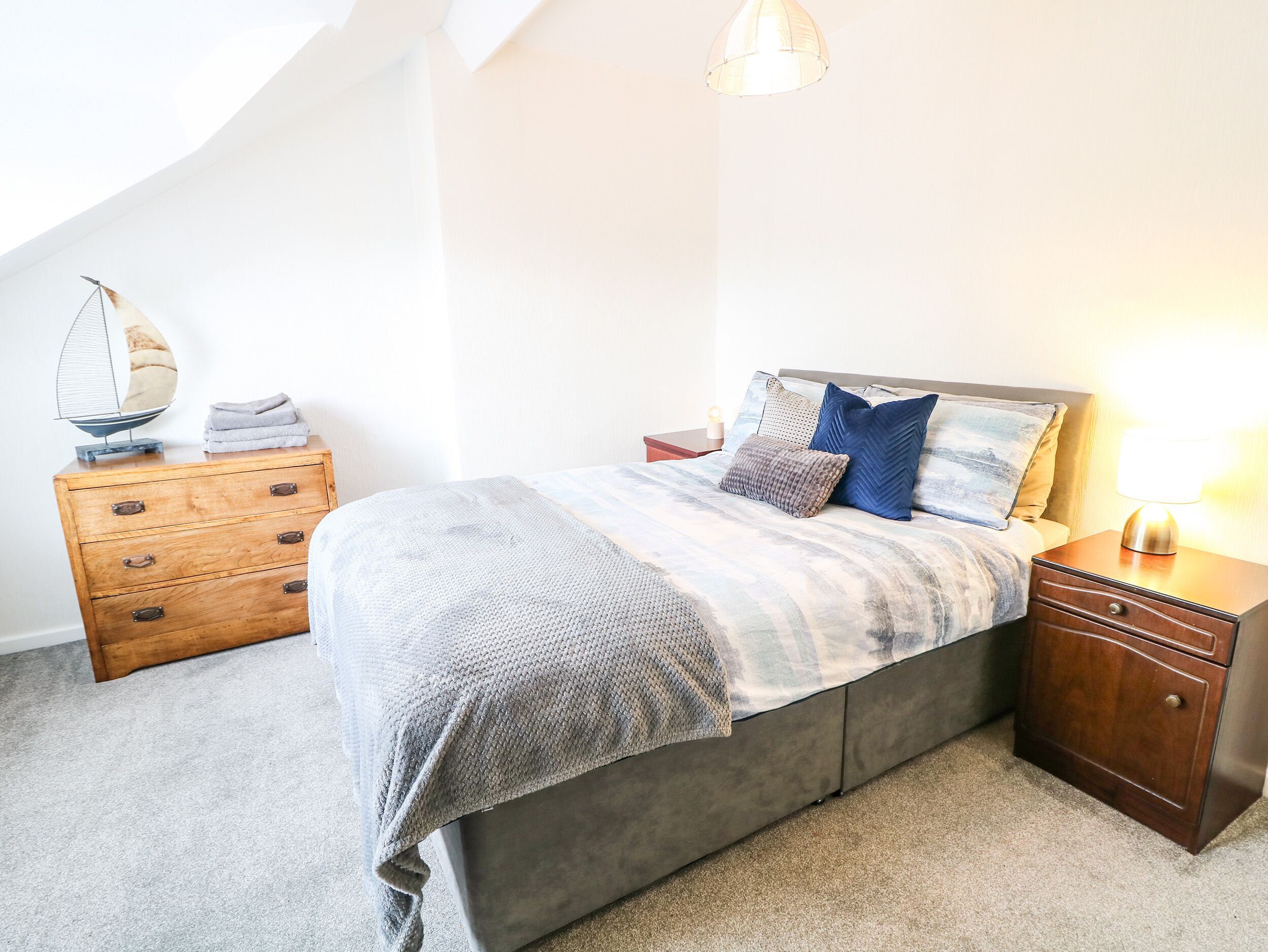 A bedroom with a bed, wooden nightstand, and a dresser.