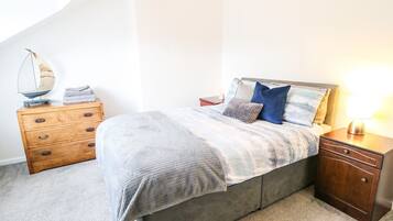 Un dormitorio con cama, mesita de noche de madera y cómoda.