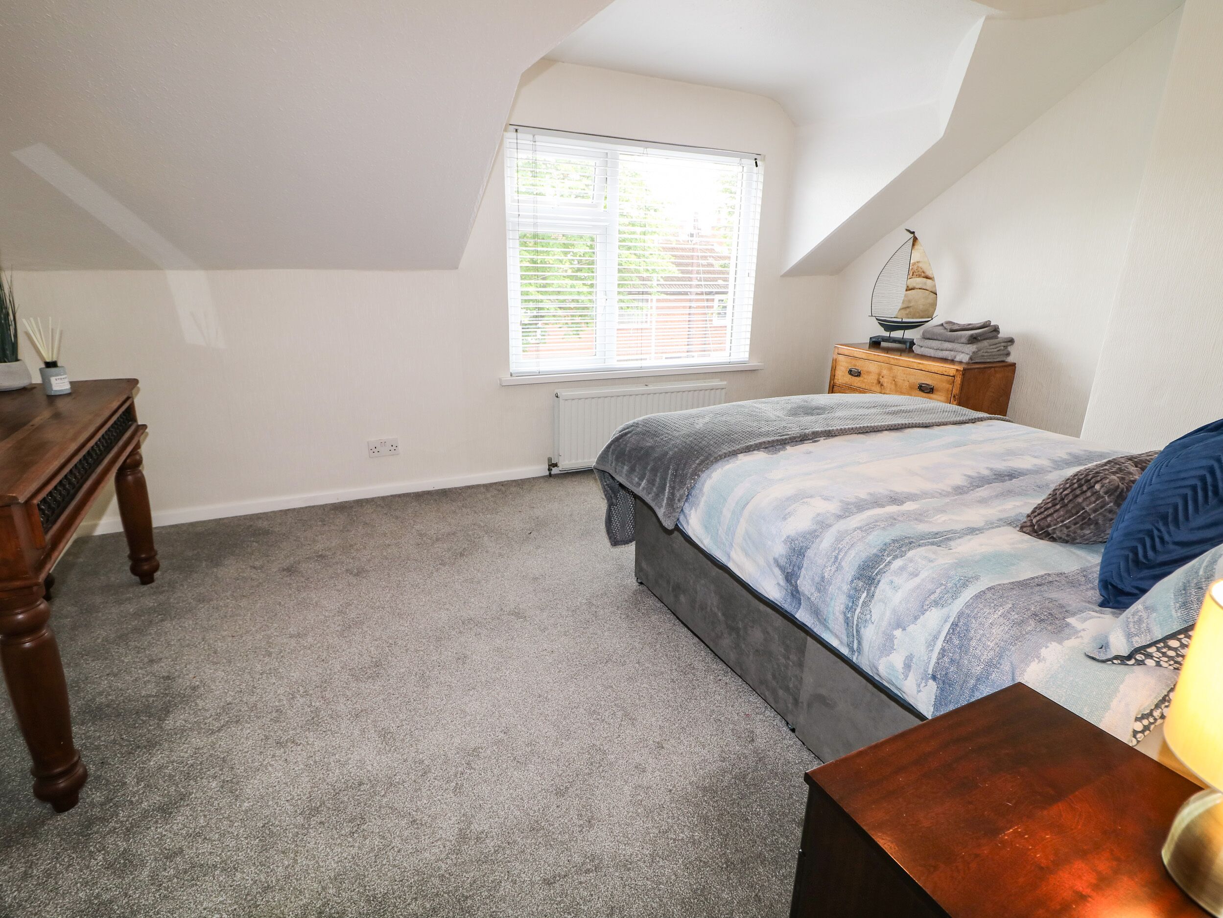 A bedroom with a bed, a dresser, a nightstand, a window, and a radiator.