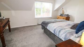 Une chambre à coucher comprenant un lit, une commode, une table de chevet, une fenêtre et un radiateur.
