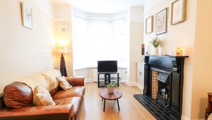 Een woonkamer met een leren bank, een klein rond tafeltje met een plant, een open haard en een televisie in de hoek.