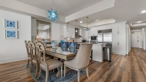 Una cocina moderna con armarios blancos, electrodomésticos de acero inoxidable y una zona de comedor con mesa y sillas de madera.