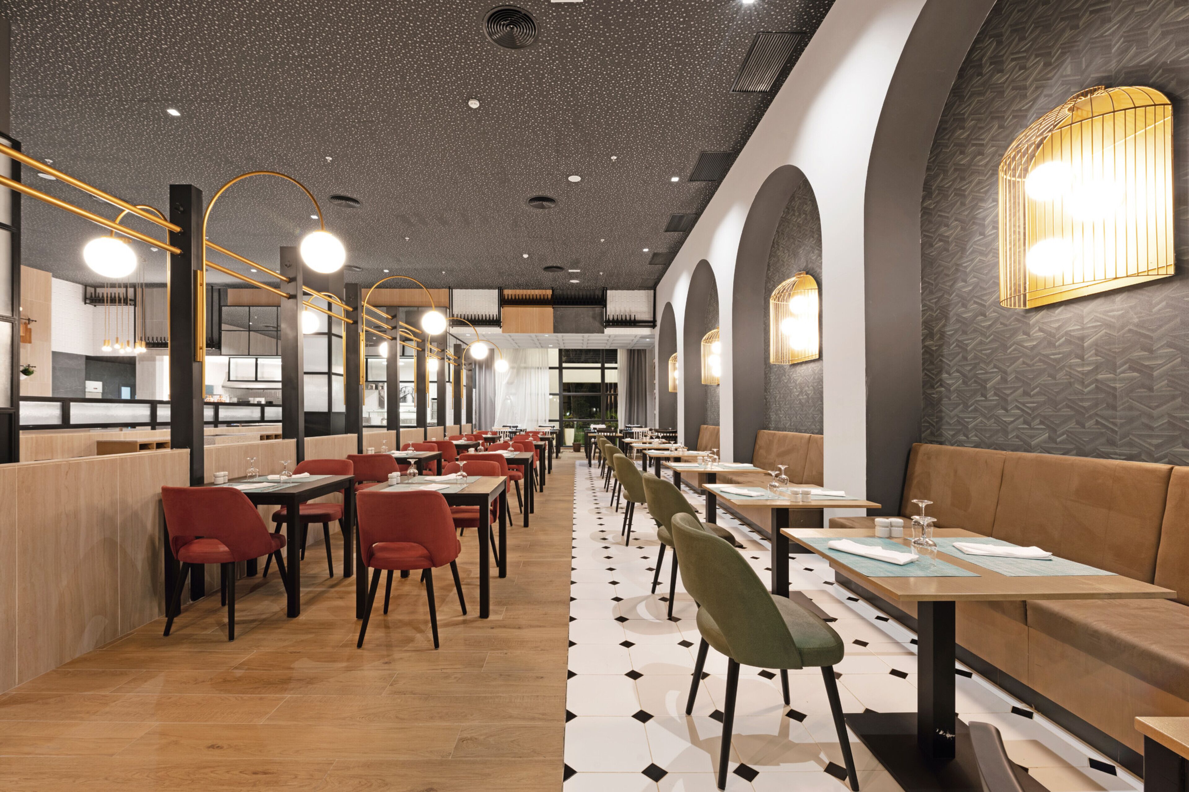 A modern restaurant interior with long tables and booths, a patterned floor, and decorative lighting.