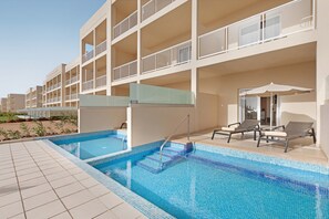 A swimming pool with steps leading into it, surrounded by lounge chairs and umbrellas.