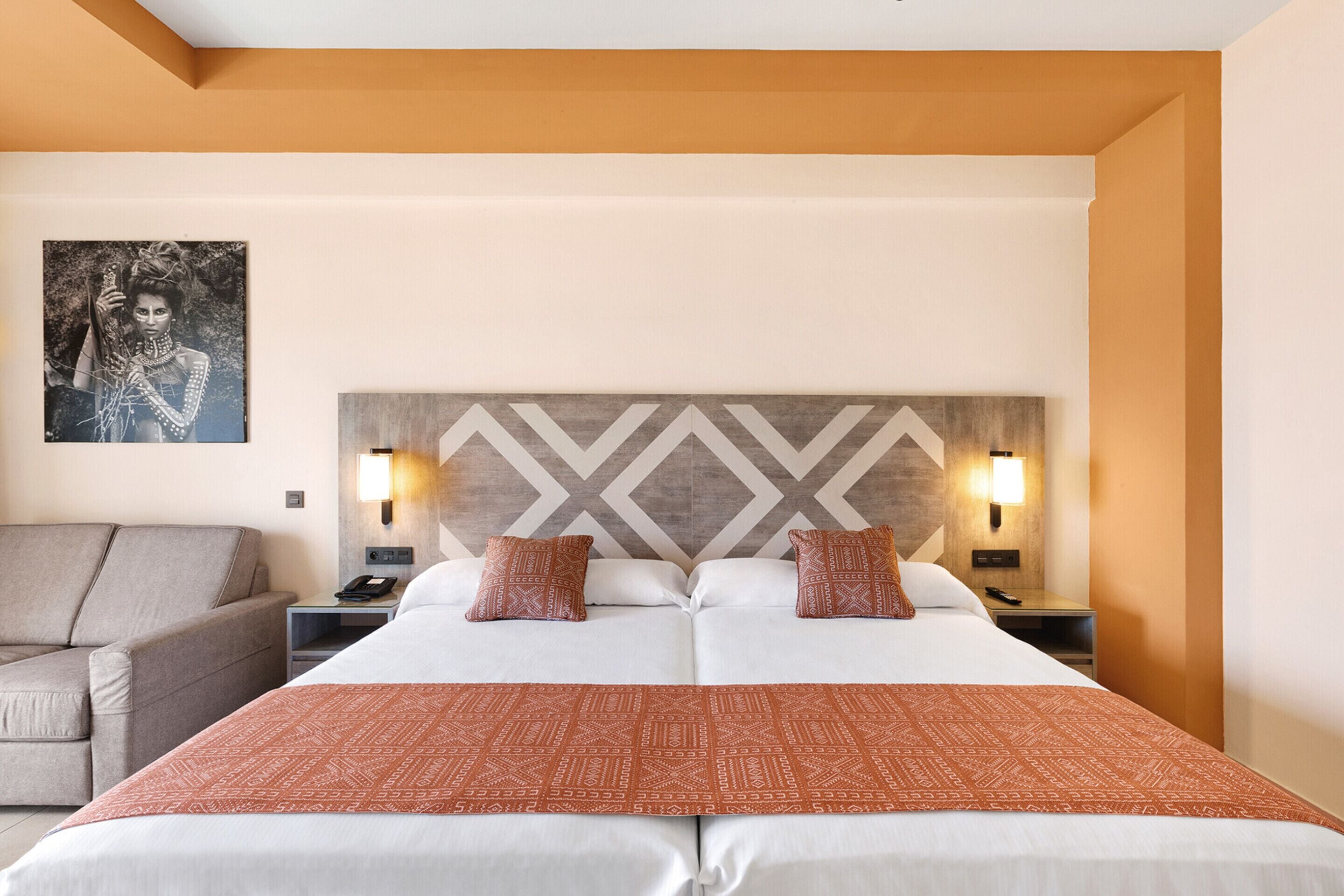 Une chambre d’hôtel avec un grand lit, deux tables de chevet avec des lampes, un canapé et une œuvre d’art accrochée au mur.