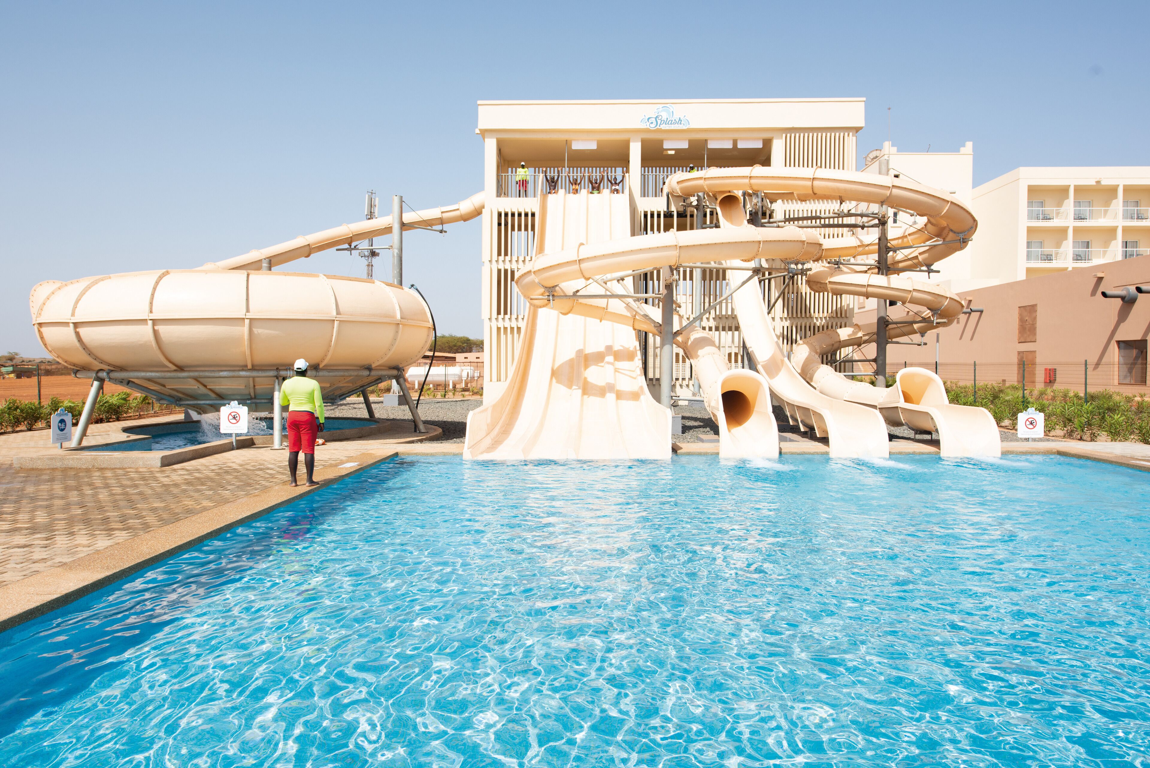 A swimming pool with a water slide and a lifeguard.