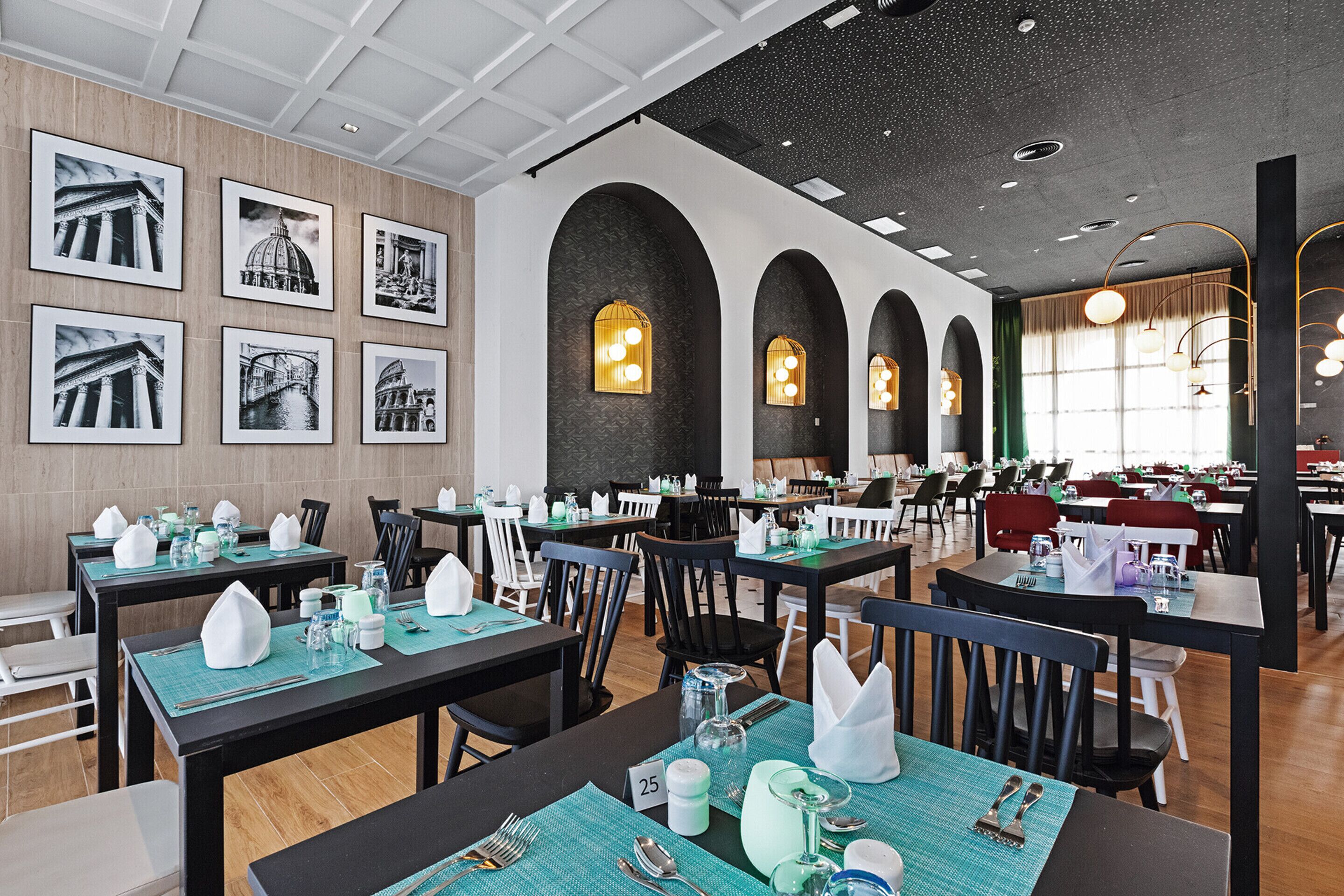 A restaurant with tables set for dining, framed pictures on the walls, and a modern ceiling design.