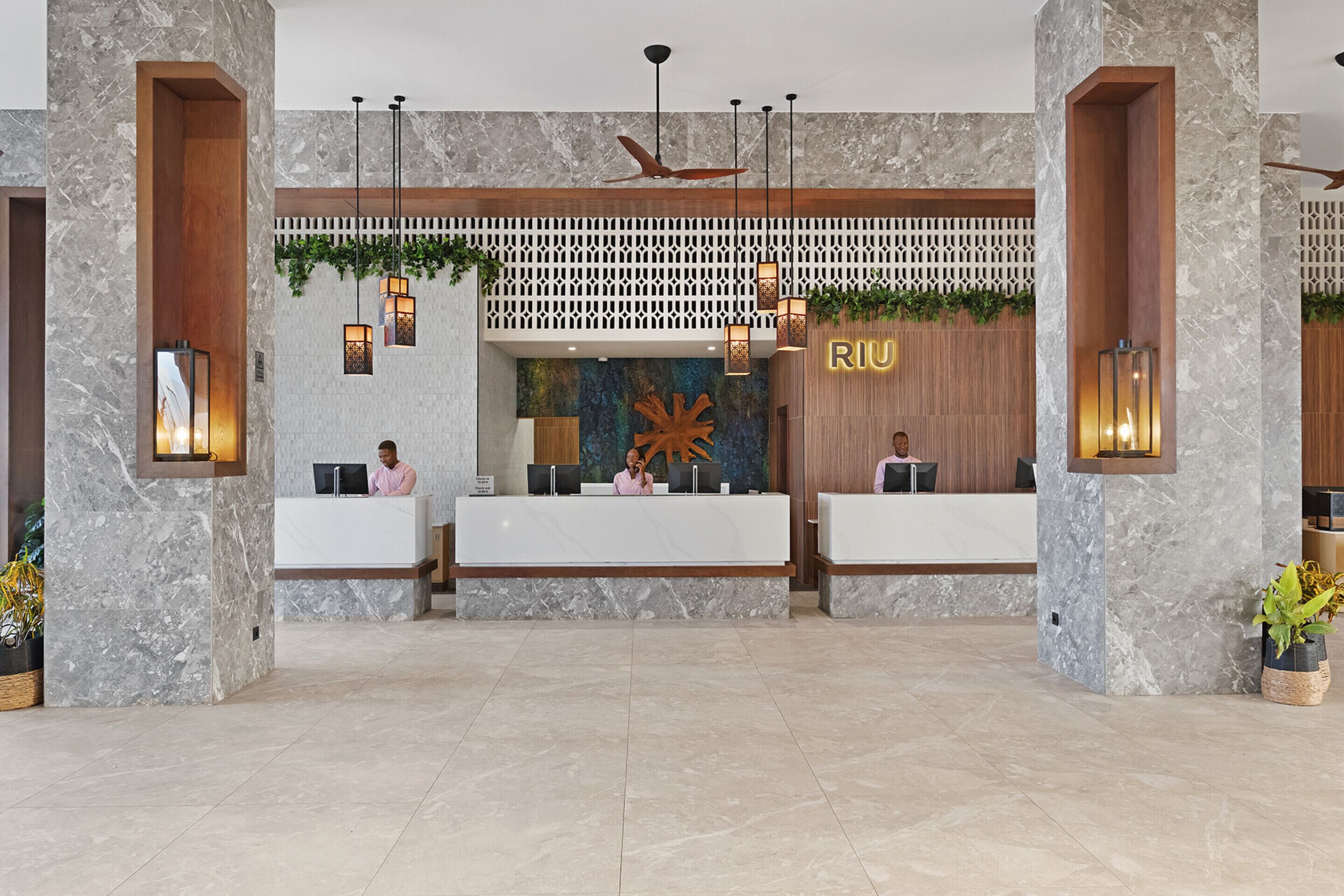 A reception area with marble walls, wooden accents, and a large 'RIU' sign.