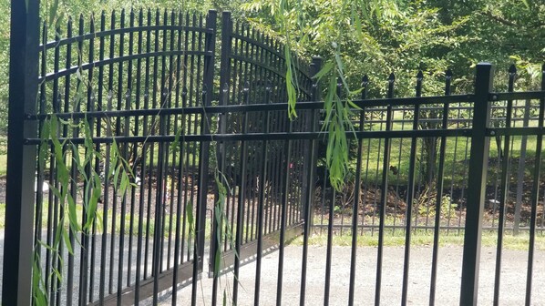A metal gate with vertical bars and a curved top, surrounded by greenery.