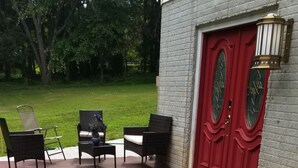 Un patio con suelo de piedra, una puerta roja y mobiliario exterior.