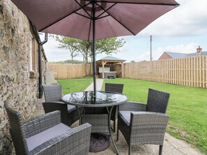 A patio with a round table and wicker chairs, a purple umbrella, and a wooden fence. - Sportsmans Lodge (Kirriemuir)