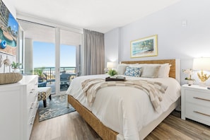 A hotel room with a bed, a nightstand, a desk, a chair, a balcony with a view, and a painting on the wall. - Avista Resort 220-3BR/3BA Oceanfront Condo in Ocean Drive (North Myrtle Beach)