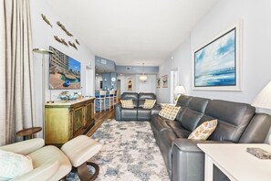 A living room with a sofa, chairs, a coffee table, a poolside view, and a dining area with chairs and a table. - Avista Resort 220-3BR/3BA Oceanfront Condo in Ocean Drive (North Myrtle Beach)