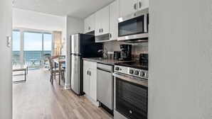 A modern kitchen with stainless steel appliances, a dining area with a view of the ocean, and a balcony with outdoor seating. - Avista Resort 823-1BR/1BA Oceanfront Condo in Ocean Drive (North Myrtle Beach)