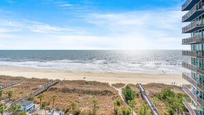 A beach view with a boardwalk, beach umbrellas, and a building with balconies overlooking the ocean. - Avista Resort 823-1BR/1BA Oceanfront Condo in Ocean Drive (North Myrtle Beach)