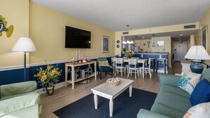 Una sala de estar con un sofá, una mesa de centro, un televisor y una cocina al fondo.