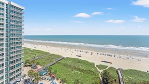 Un grand hôtel situé dans un immeuble de grande hauteur, offrant une vue sur une plage, une promenade en bord de mer et des parasols de plage.