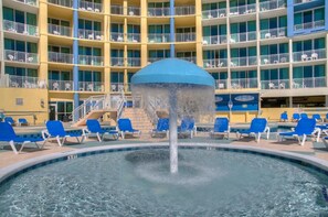 Une piscine d’hôtel avec une fontaine centrale et des chaises longues bleues disposées autour.