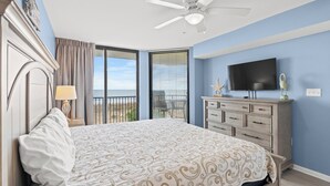 Un dormitorio con cama, ventilador de techo, televisión, cómoda y balcón con vistas.